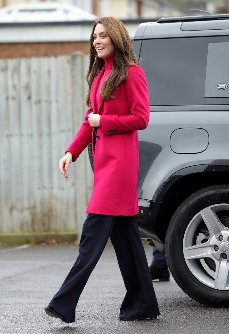 Kate Middleton marchant dehors avec une veste rose vif et un pantalon bleu foncé